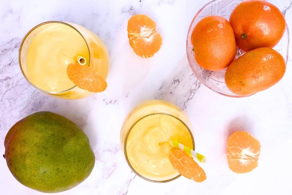 overhead view of orange mango smoothie glasses with fresh fruit