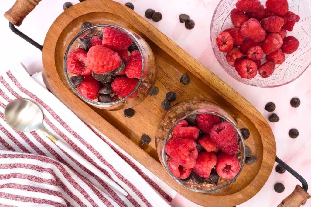 overhead view of raspberry chocolate overnight oats in a glass with fresh fruit and chocolate surrounding