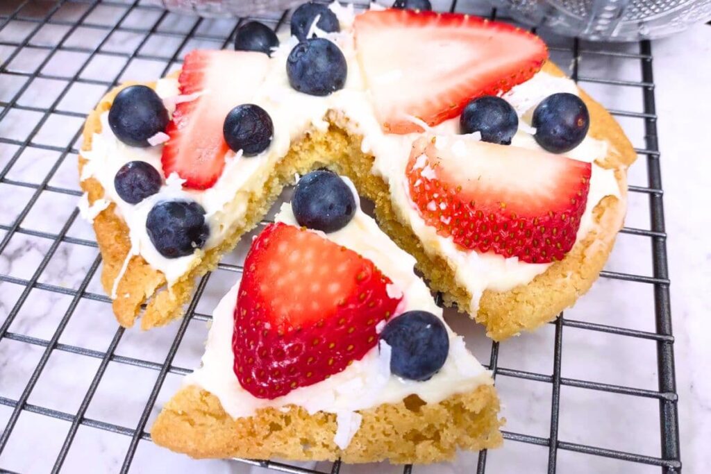 slice cut from a sugar cookie fruit pizza with strawberry and blueberry