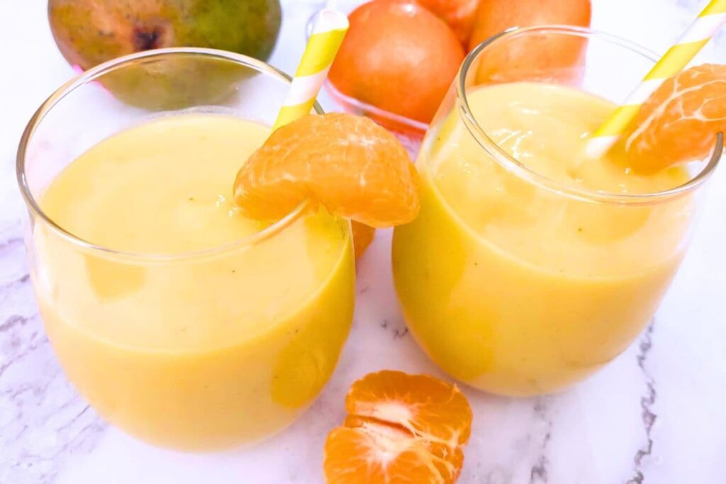 two glasses of orange mango smoothie with a slice of fresh orange