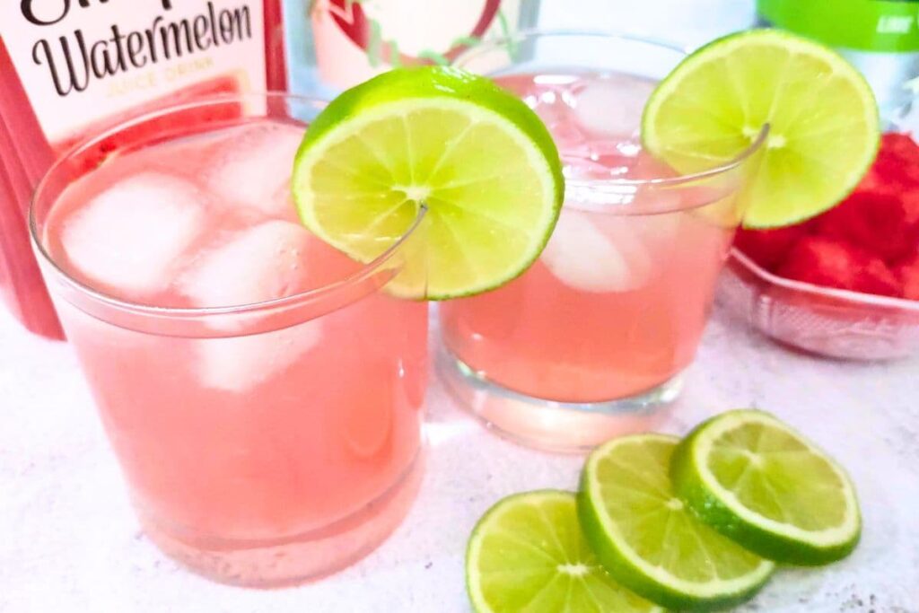 two highball glasses filled with watermelon gin fizz cocktail garnished with lime slice
