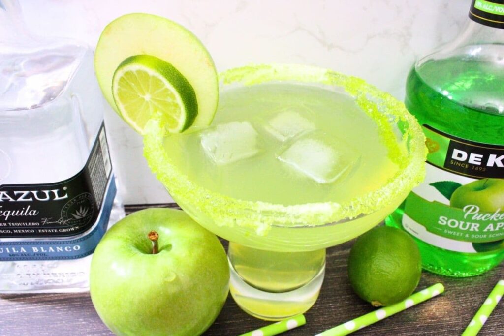 large sour green apple margarita with fruit garnish and liquor bottles