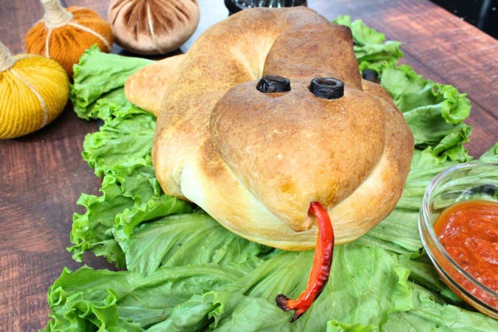 snake calzone on a bed of lettuce facing the camera with red pepper tongue sticking out