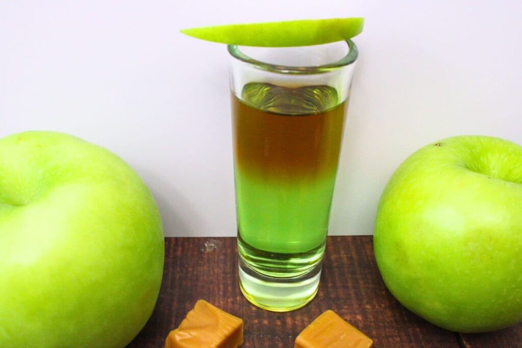 caramel apple shot next to two apples with a slice on top