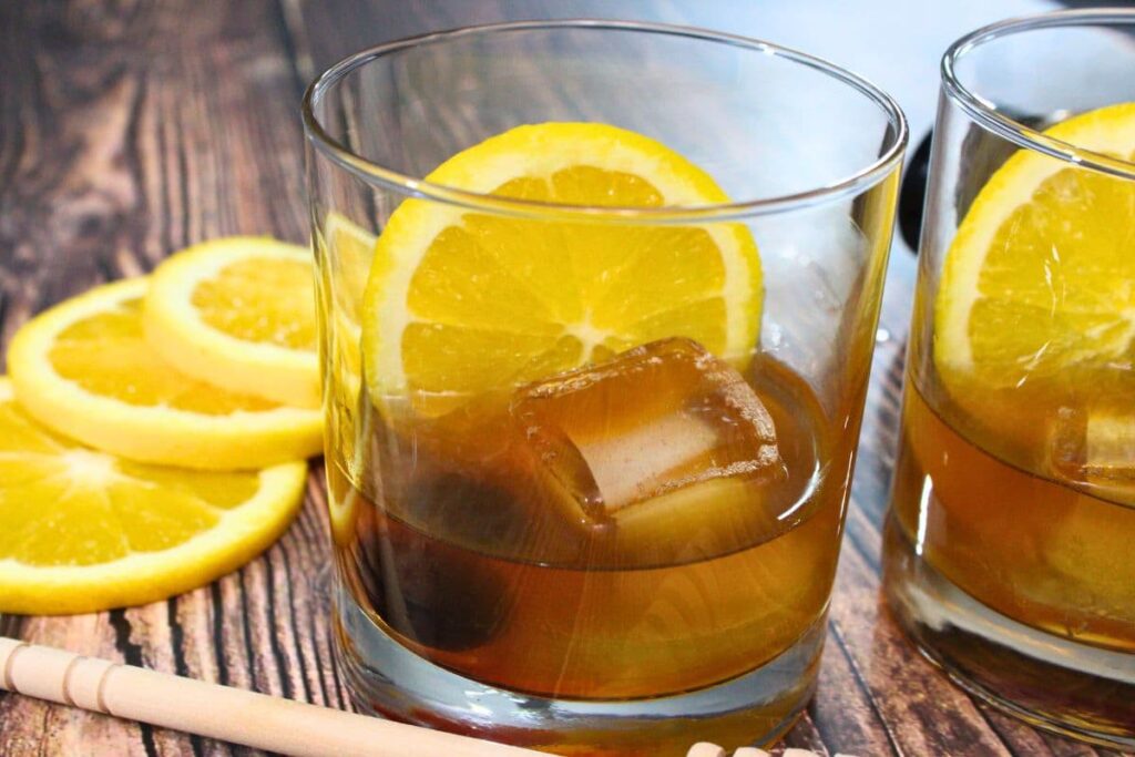 glass of hot honey old fashioned surrounded by fresh orange slices