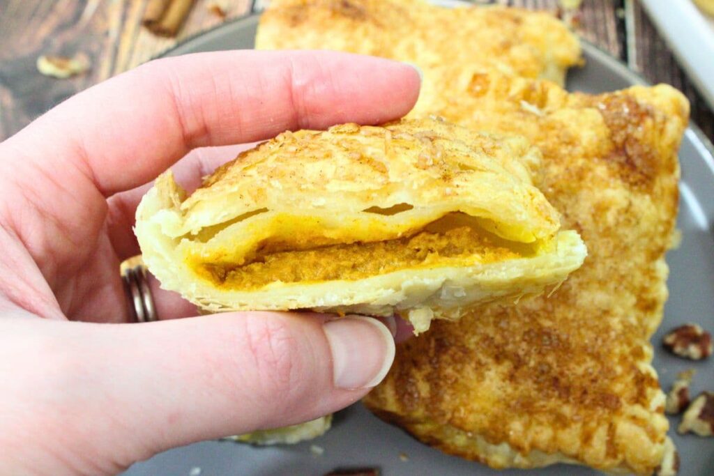 holding up a cut in half air fryer puff pastry hand pie with pumpkin filling