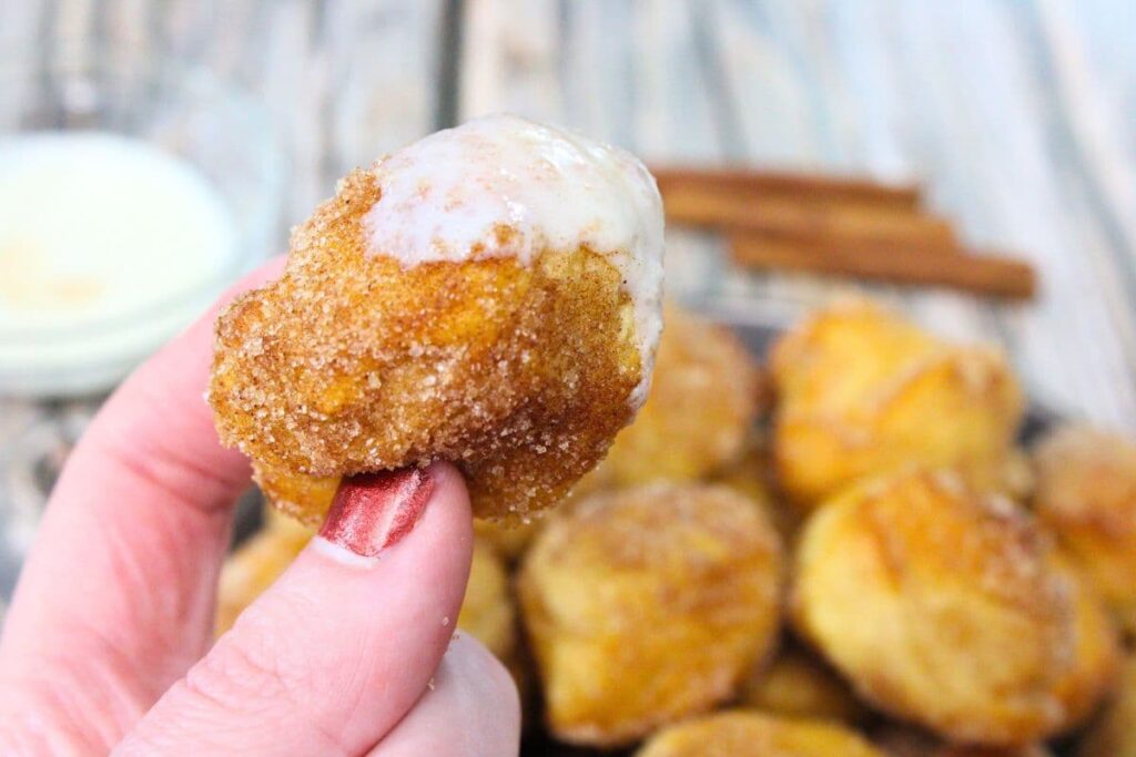 holding up an air fryer cinnamon roll bite with vanilla icing
