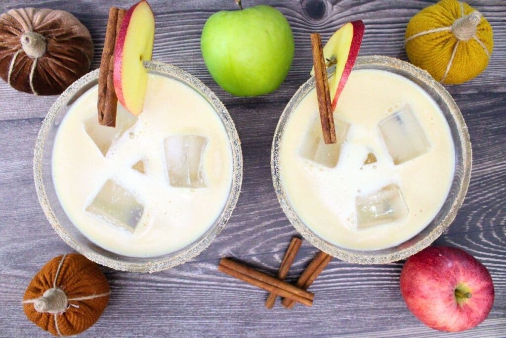 overhead view of two glasses filled with caramel apple cider margaritas and fresh fruit surrounding