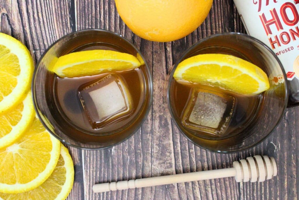 overhead view of two glasses filled with hot honey old fashioned with fresh orange slices around