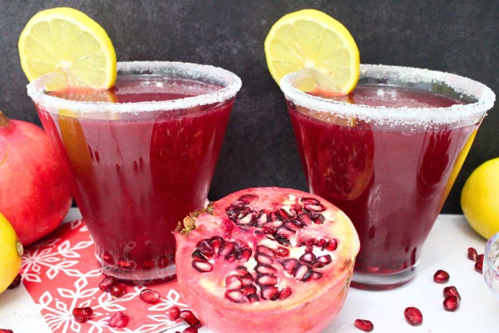 two pomegranate lemon drop martini with lemon slices against a dark background