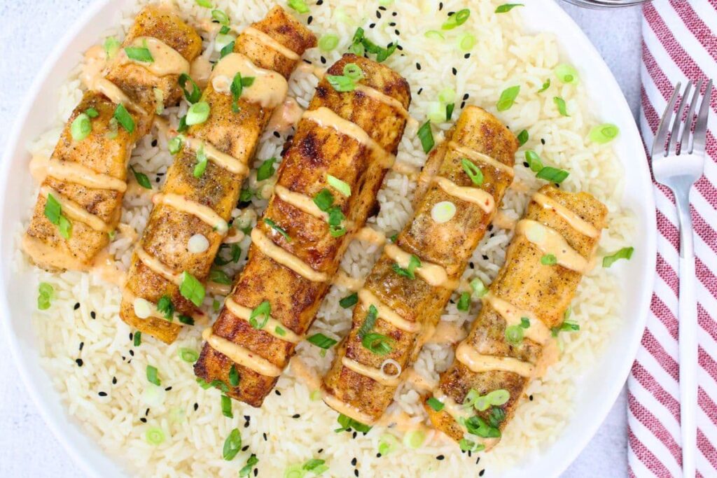 overhead view of strips of air fryer bang bang salmon on a plate with rice