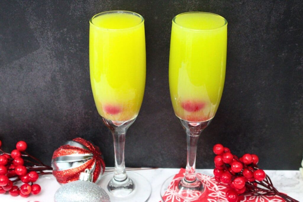 two festive grinch mimosa cocktails against a black background