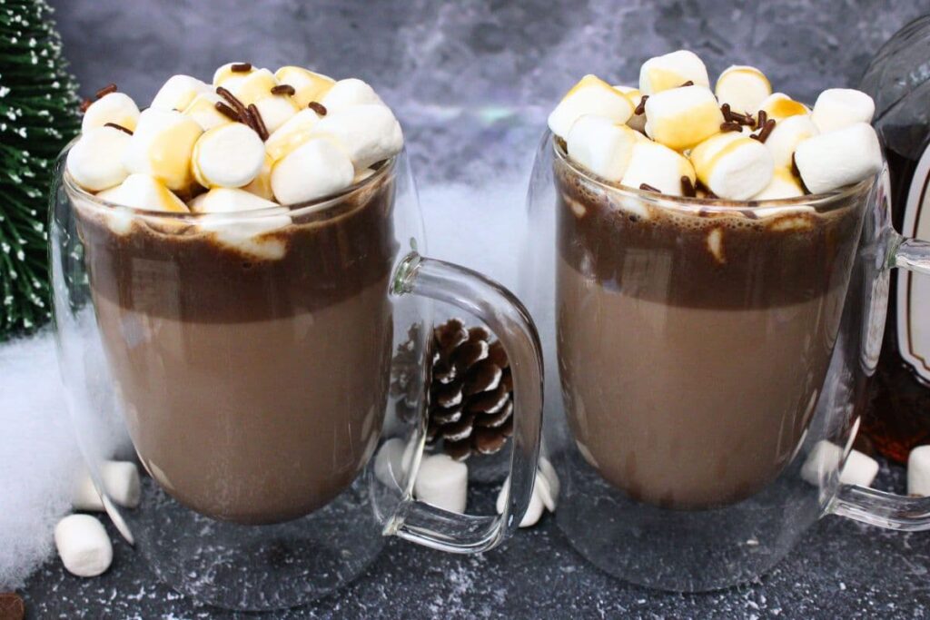 two glass mugs filled with salted caramel whiskey hot chocolate and marshmallows