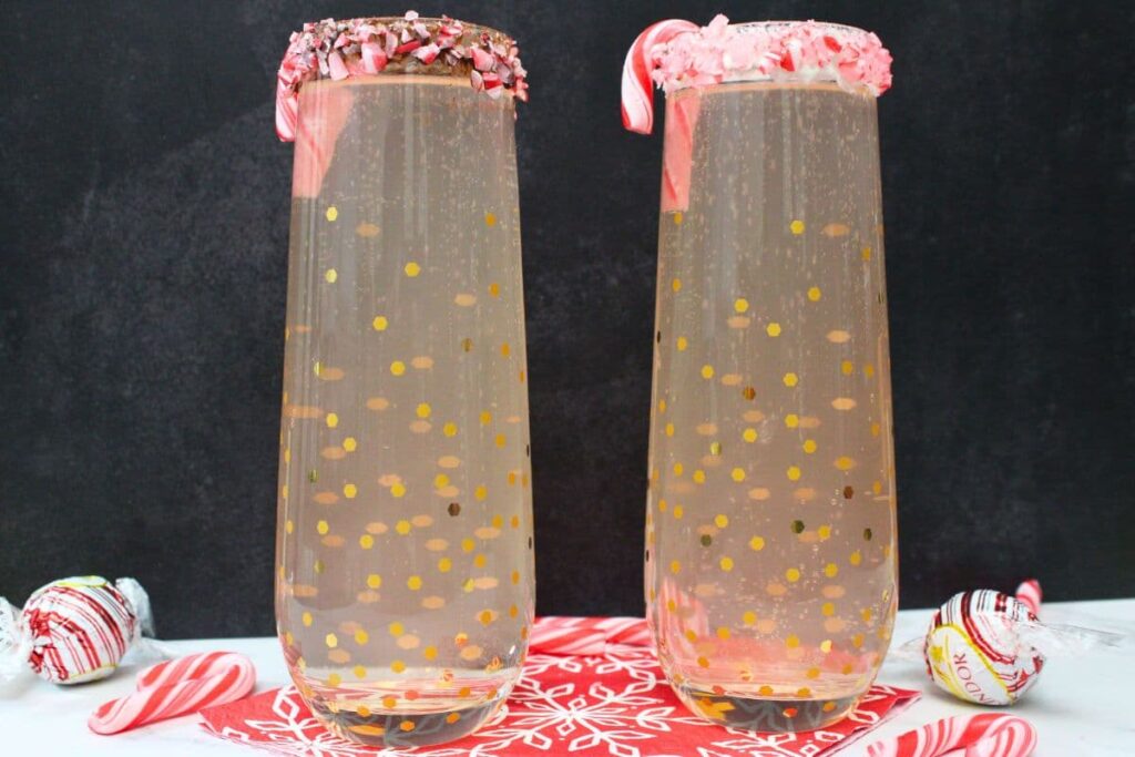 two peppermint bark mimosas in champagne glasses against a black background
