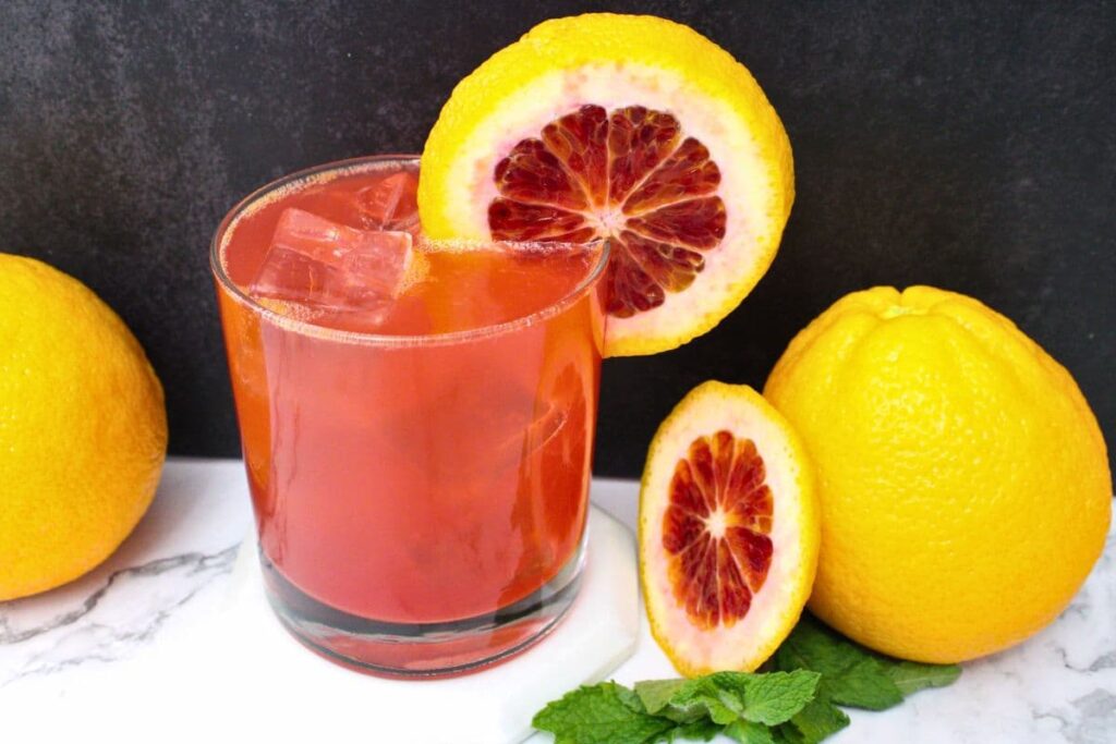 blood orange gin fizz cocktail with fresh fruit against a dark background