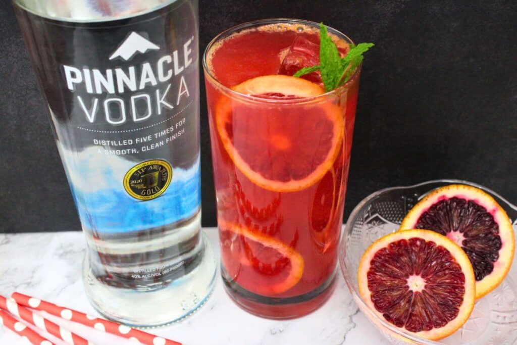 blood orange vodka cocktail in a tall glass next to a vodka bottle