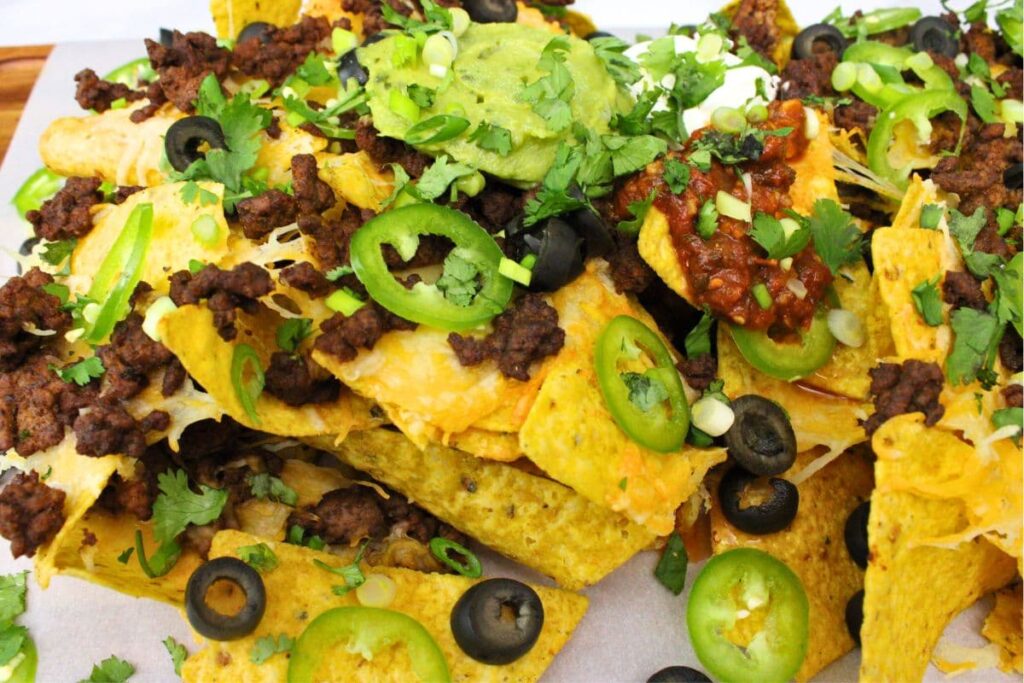 closeup of air fryer nachos topped with beef, jalapenos, olives, guacamole, and sour cream