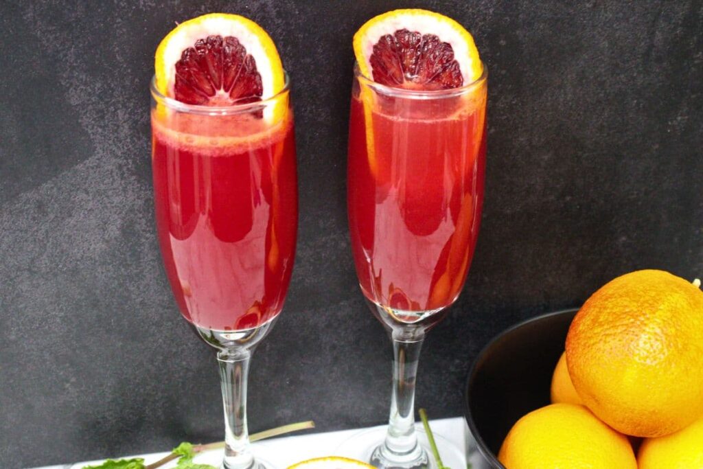 closeup view of two blood orange mimosas in champagne flutes with blood orange slices in the rim