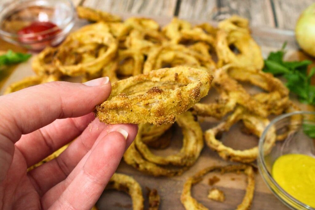 holding up a beer battered onion ring cooked in the air fryer