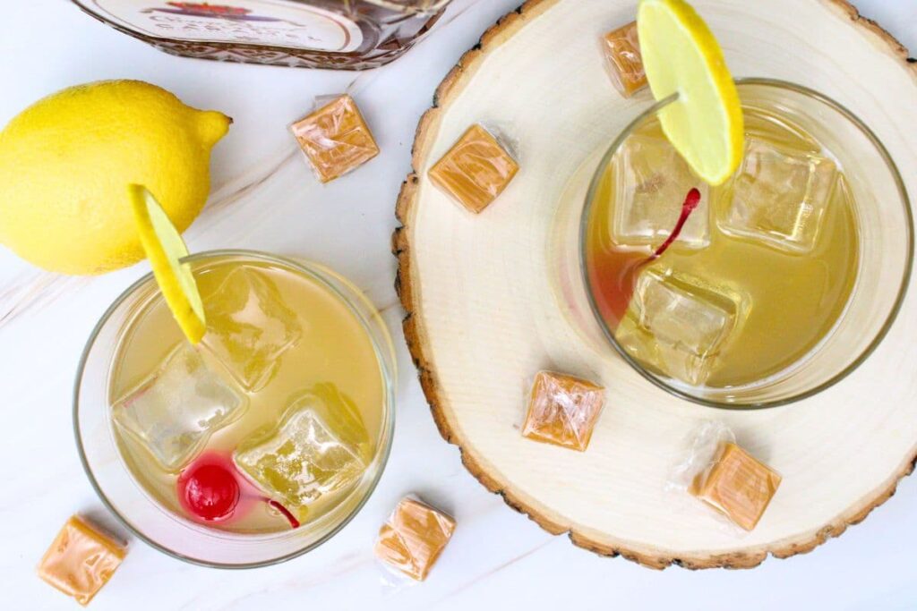 overhead view of two salted caramel whiskey sour cocktails with caramel cubes surrounding