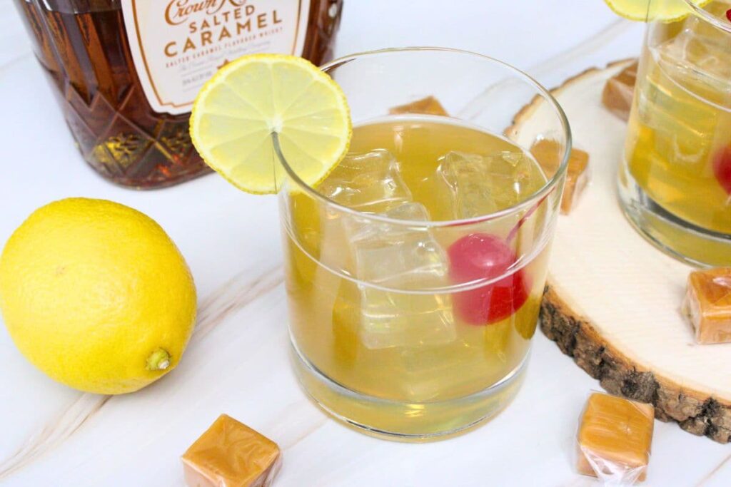 salted caramel whiskey sour with a lemon slice in the rim and the bottle in the back