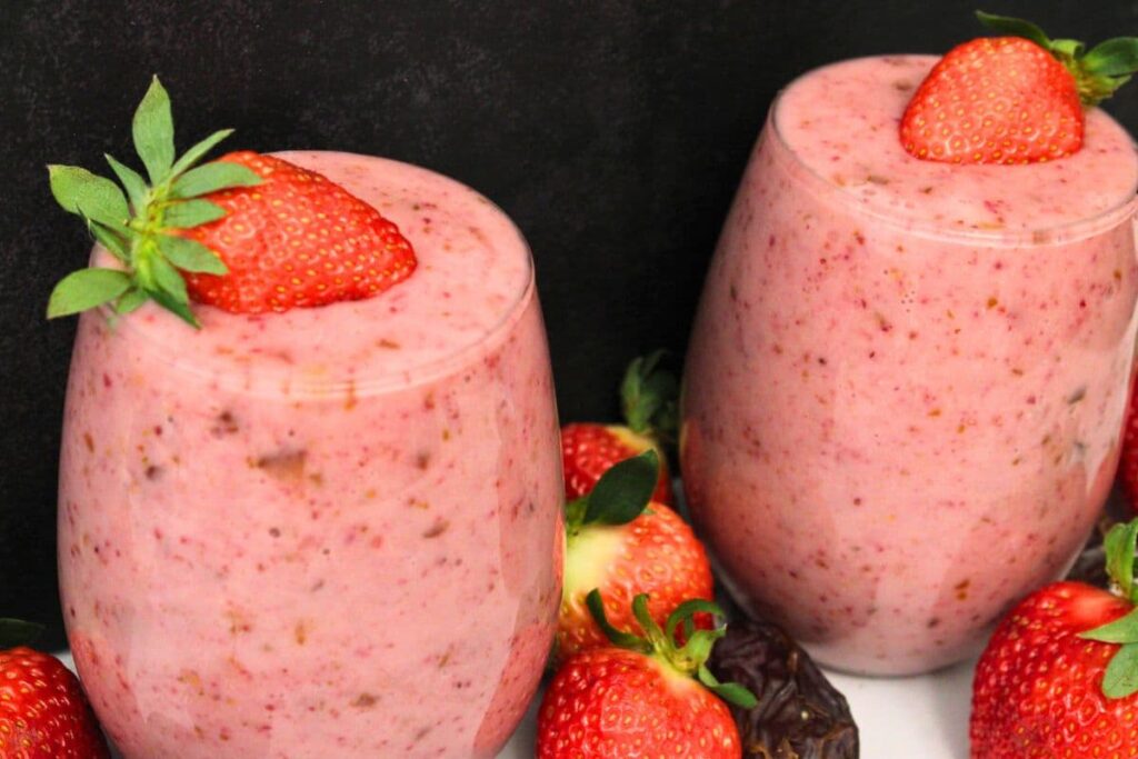 strawberry date smoothies topped with fresh strawberries against a dark background
