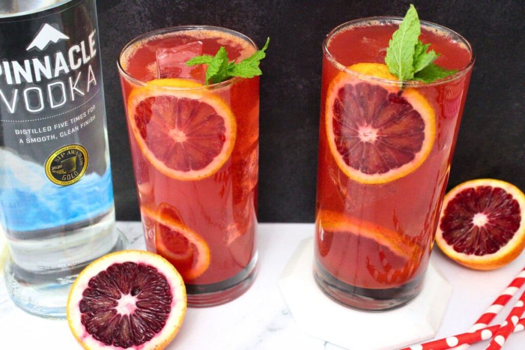 two glasses of blood orange vodka cocktails in tall glasses with blood orange slices