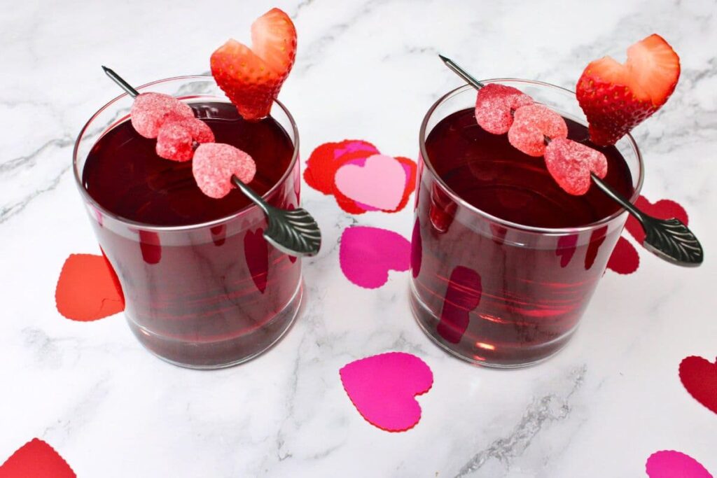 two love potion cocktails in rocks glasses with gummy skewer and heart shaped strawberries