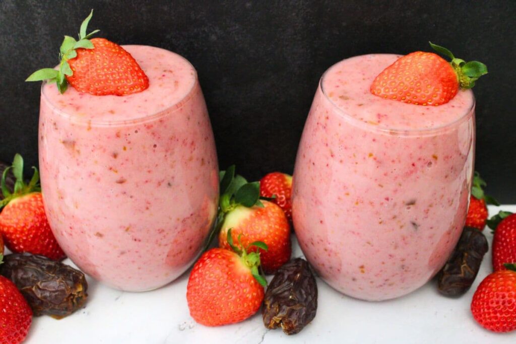 two strawberry date smoothies surrounded by fresh dates and strawberries