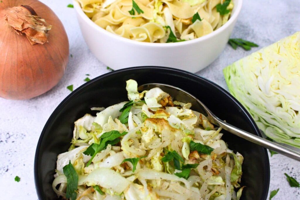 dipping a spoon into a bowl of air fryer cabbage and onions with a bowl of haluski above