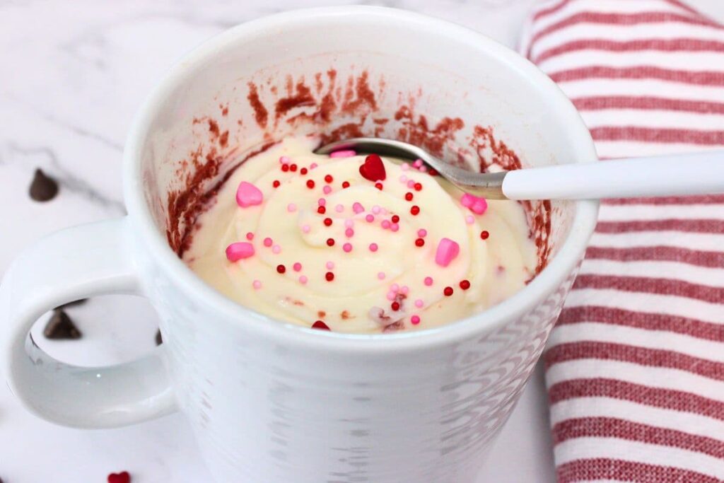 dipping a spoon into red velvet mug cake with cream cheese frosting