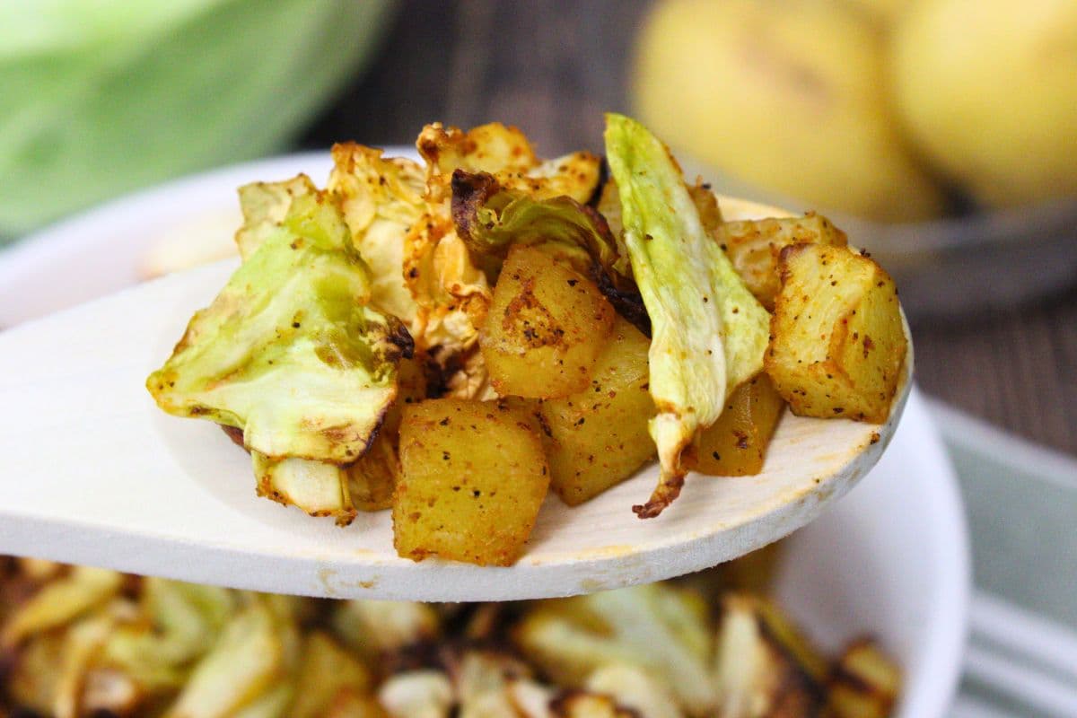 holding up a wooden spoon with air fryer cabbage and potatoes