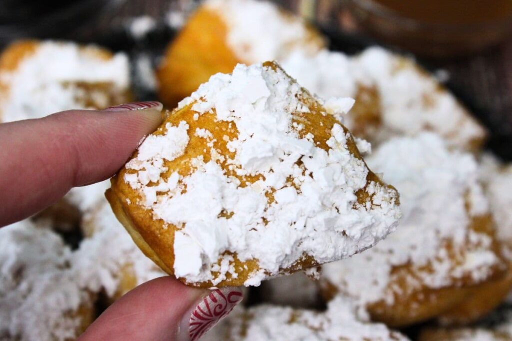 holding up an air fryer biscuit beignet coated in powdered sugar