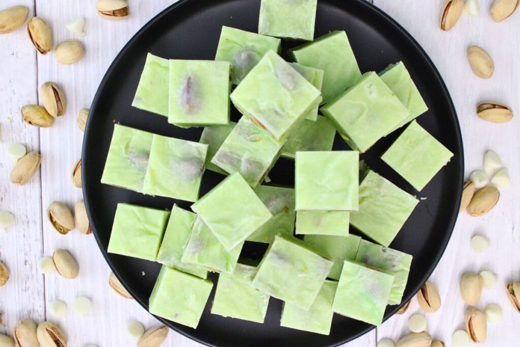 overhead view of pistachio fudge cubes stacked on a black plate