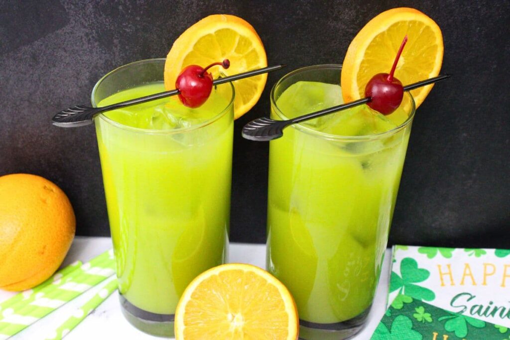 two glasses of drunken leprechaun cocktails with fresh orange slices against a black background