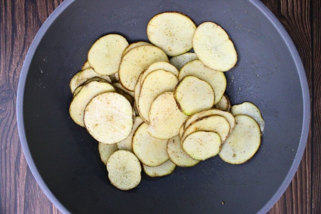add potato slices to a bowl with olive oil, salt, pepper, and garlic powder