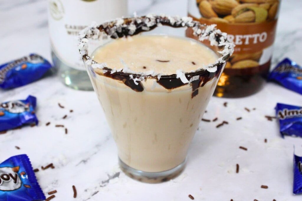 almond joy martini with a chocolate coconut rim in front of liquor bottles