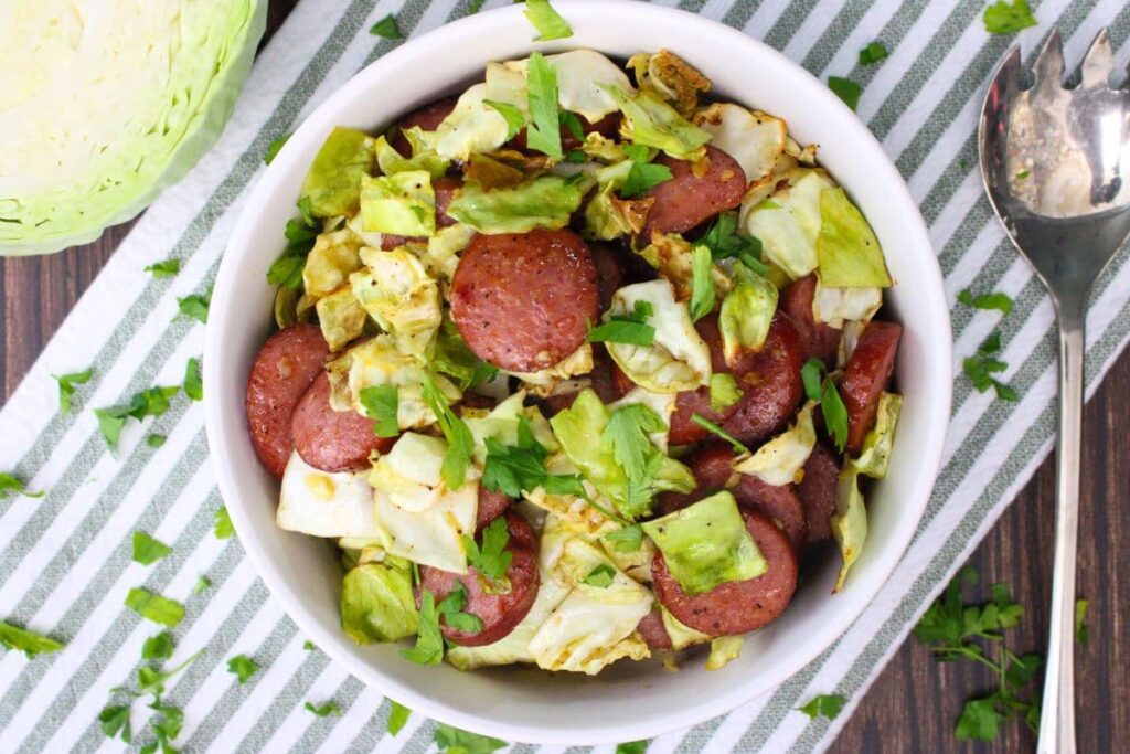 overhead view of air fryer cabbage and sausage in a bowl with a serving spoon