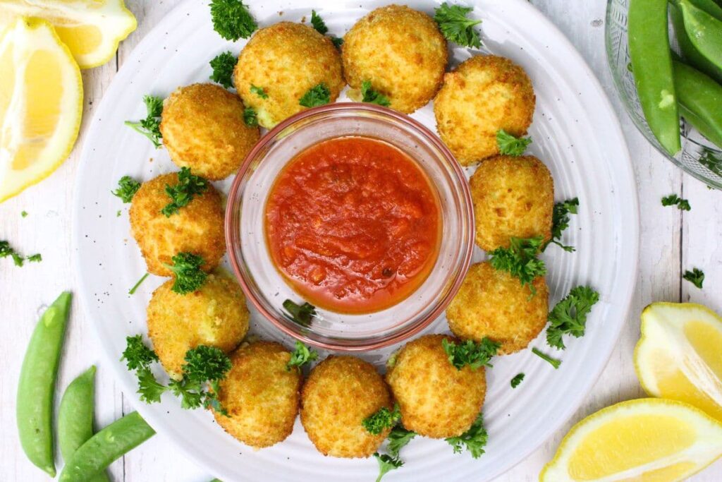 overhead view of air fryer frozen arancini on a plate circling a dish of marinara