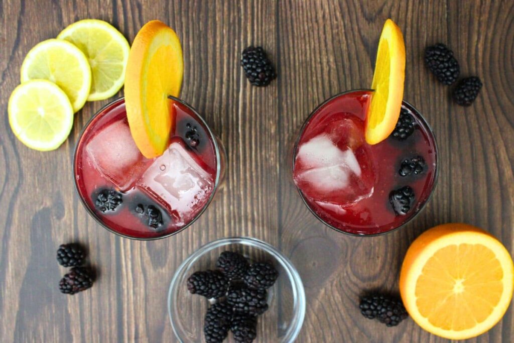overhead view of two blackberry rambler drinks with fresh fruit slices