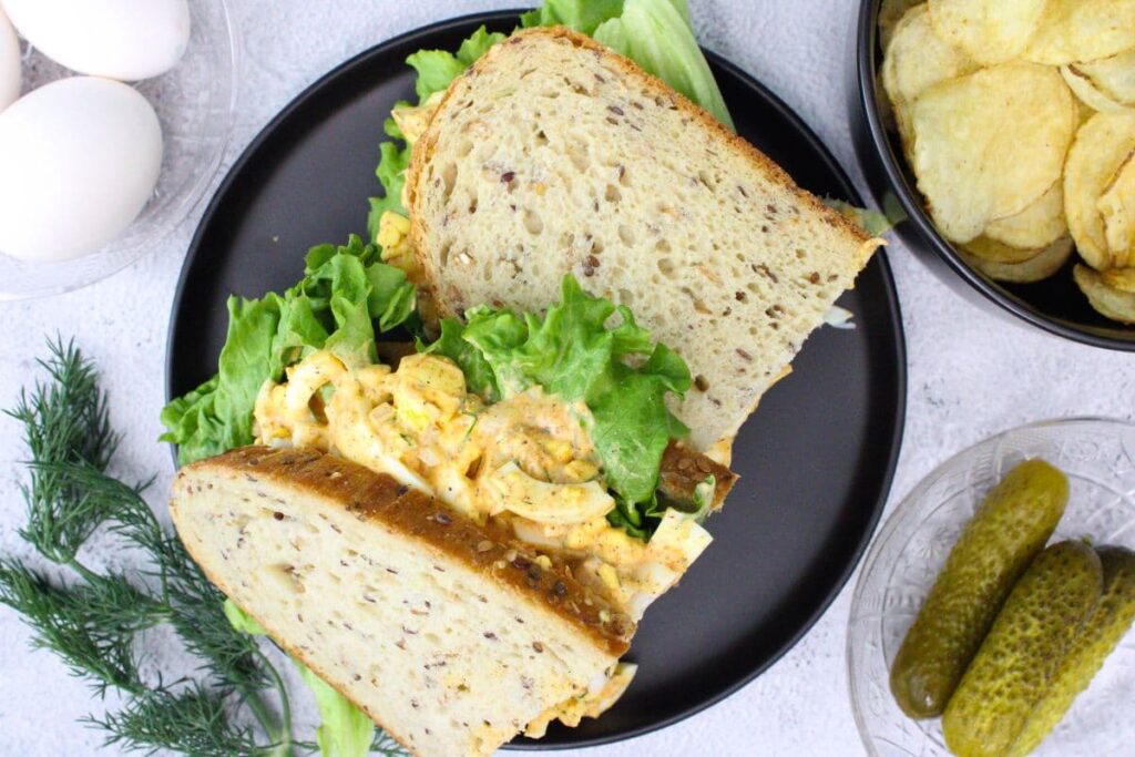overhead view of two halves of an air fryer egg salad sandwich with lettuce on a black plate