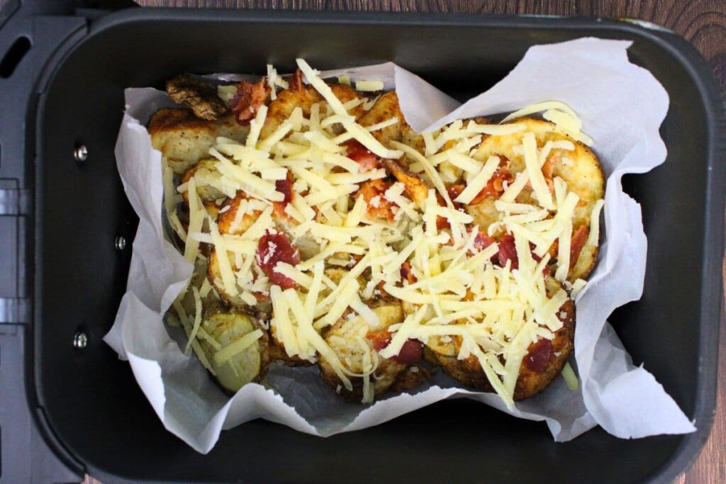 place fried potatoes in air fryer basket and top with cheese and bacon