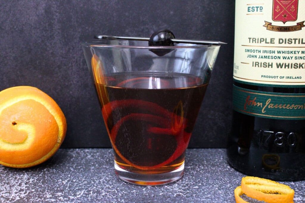 tipperary cocktail with orange twist and cherry against a dark background