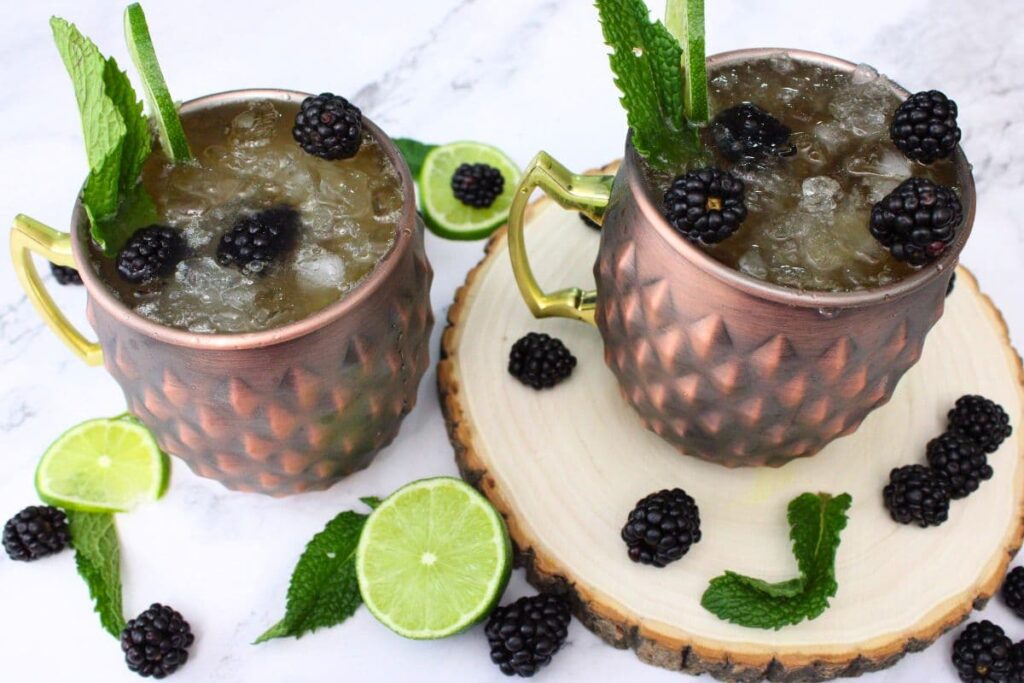 two blackberry kentucky mule cocktails with fresh lime and blackberries surrounding the mugs