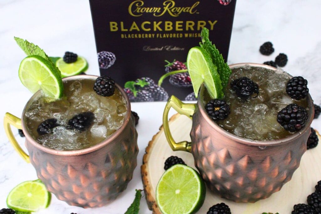 two copper mugs filled with crown royal blackberry kentucky mules in front of crown royal box