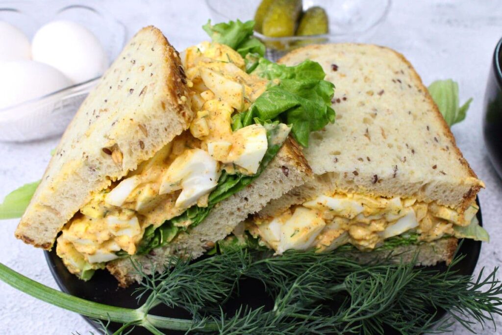 two halves of an air fryer egg salad sandwich on a black plate with fresh dill