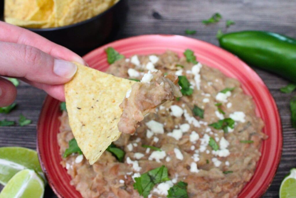 holding up a chip dipped in air fryer refried beans