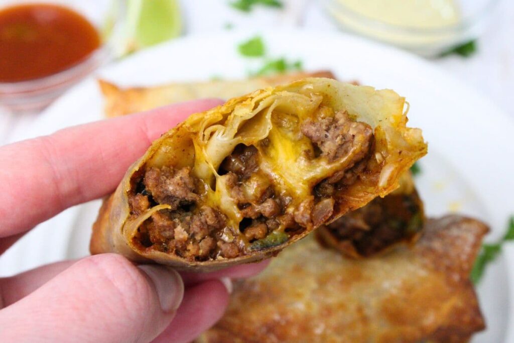 holding up half of an air fryer taco egg roll to show the beef and cheese filling