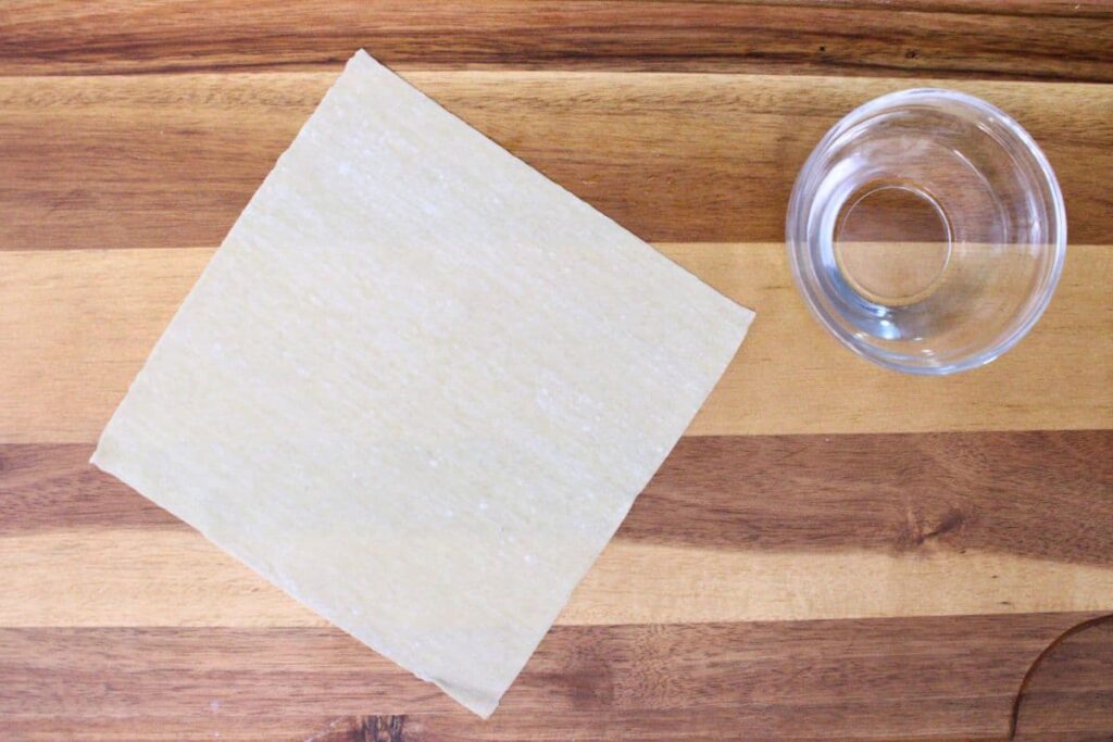 lay egg roll wrapper and a small dish of water on a cutting board