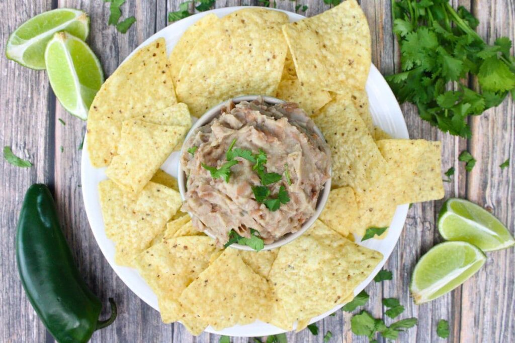 overhead view of a dish filled with refried beans surrounded by tortilla chips